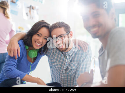 Portrait creative business people with headphones hugging in sunny office Stock Photo