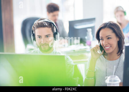 Creative business people with headphones talking on cell phone and using computer in office Stock Photo