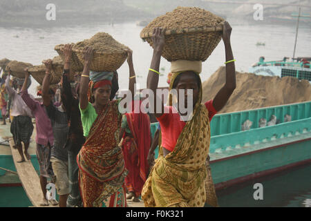 Male and female laborers carry heavy loads of sand balanced on their heads in the Bank of Turag River at Gabtoli in Dhaka. Stock Photo