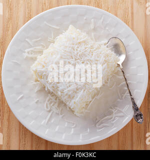 Brazilian traditional dessert: sweet couscous (tapioca) pudding (cuscuz doce) with coconut on white plate on wooden table. Selec Stock Photo