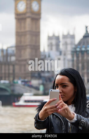 An attractive dark haired girl takes a 'selfie' with London's famous Big Ben and the Thames river in the background. Stock Photo