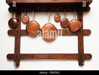 Group of vintage copper pans, different size, hung on wooden shelf in kitchen Stock Photo