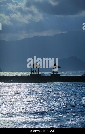 Pair of tourists, enjoying the ocean view from the shelter of their seaside pagoda in the late afternoon light. Stock Photo