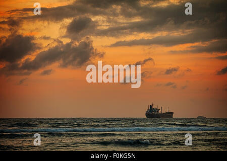 Enormous tanker ship, passing in the distance, along the horizon on this tropical sea at sunset. Stock Photo