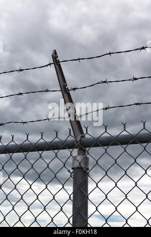 A view of the sky with dark clouds behind a barbed wire security fence. Stock Photo