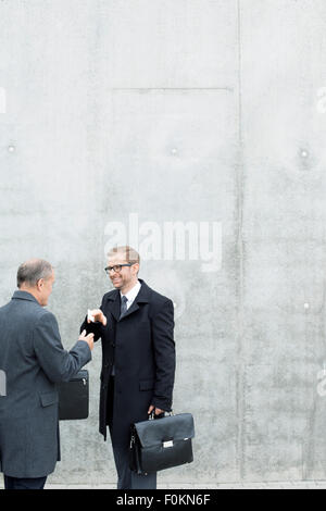 Two businessmen exchanging business cards at concrete wall Stock Photo