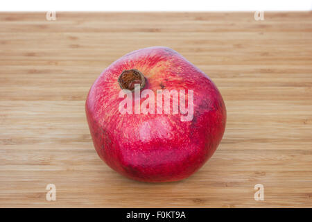 Close-up of a whole ripe pomegranate (Punica granatum) on a wooden chopping board. Stock Photo