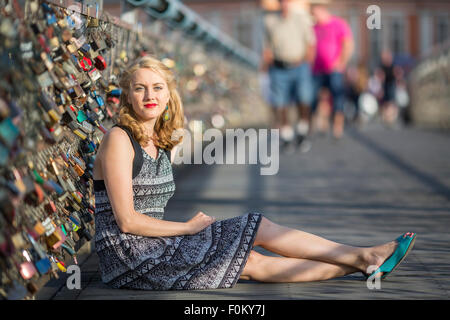 Young beautiful blond woman sitting on the bridge of love (bridge with locks) Stock Photo