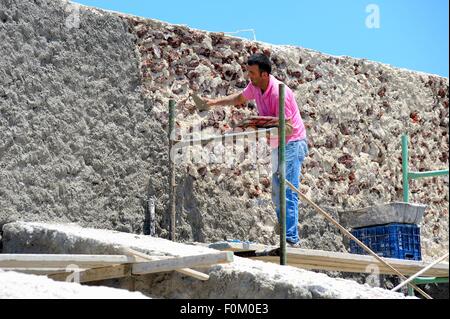 A builder applying cement to render a wall in Santorini Greece Stock Photo