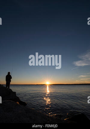 Silhouette of a young fisherman fishing at dusk Stock Photo