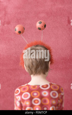 Portrait of little girl wearing fun headband with balls. She is turned away from the camera showing her back.