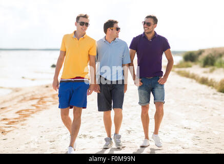 smiling friends in sunglasses walking along beach Stock Photo