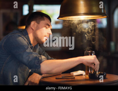 man drinking beer and smoking cigarette at bar Stock Photo