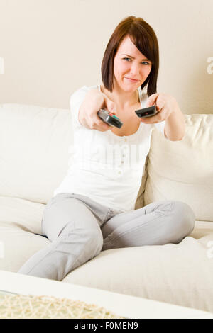 Young happy woman with two remote controls on a sofa in her living room Stock Photo