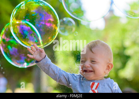 Cute baby catching soap bubbles in a summer day Stock Photo