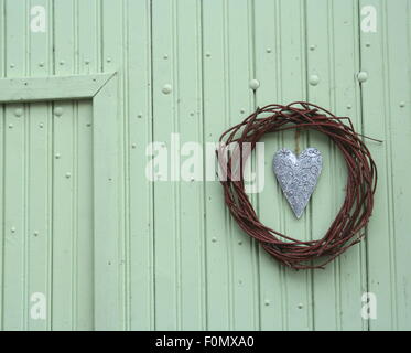 Vintage hammered tin heart in circle wreath on green wooden wall, Germany. Stock Photo