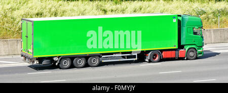 Side view of green coloured hgv lorry truck & driver cab towing a clean unmarked articulated trailer driving along M25 motorway Essex England UK Stock Photo