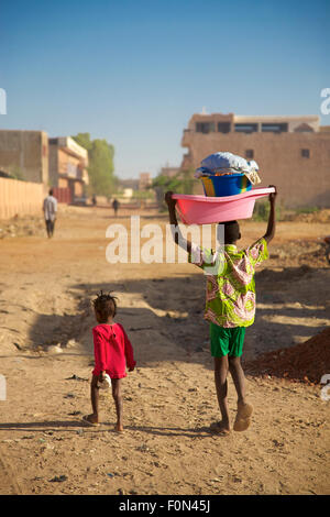 Unidentified Small kid walking in the street with his brother early in the morning carrying laundry on his head in Mopti, 2010 Stock Photo