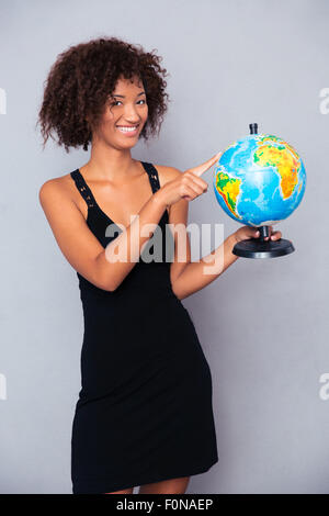 Portrait of a happy african woman holding globe over gray background Stock Photo