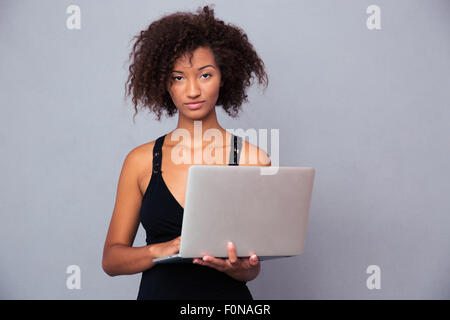 Portrait of a beautiful afro american woman using laptop over gray background. Looking at camera Stock Photo
