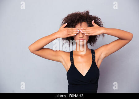 Portrait of afro american woman covering her eyes over gray background