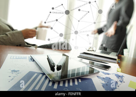 business documents on office table with smart phone and laptop and two colleagues discussing data in the background Stock Photo