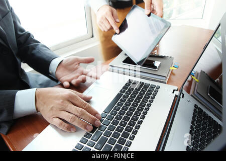 business documents on office table with smart phone and digital tablet and stylus and two colleagues discussing data in the background Stock Photo