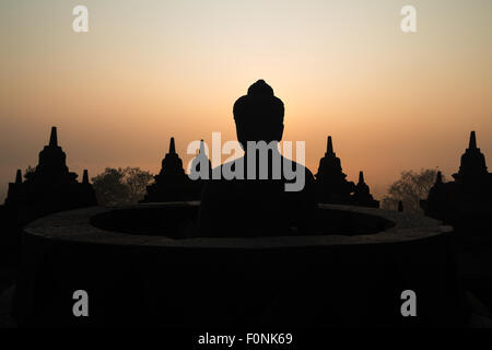 Silhouettes of a Buddha statue at the Unesco world heritage site the Borobudur temple at dawn on the island of Java, Indonesia, Asia. Stock Photo