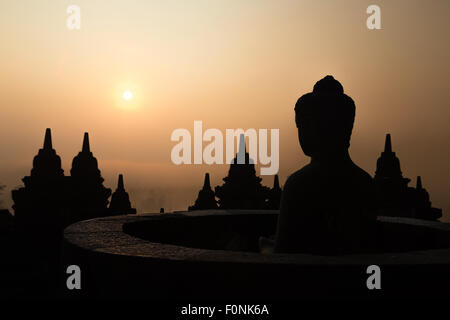 Silhouettes of a Buddha statue at the Unesco world heritage site the Borobudur temple at dawn on the island of Java, Indonesia, Asia. Stock Photo