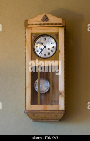 An indoor wall mounted traditional style wooden clock with pendulum and a face with numbers on in a house in Austria. Concept: time Stock Photo