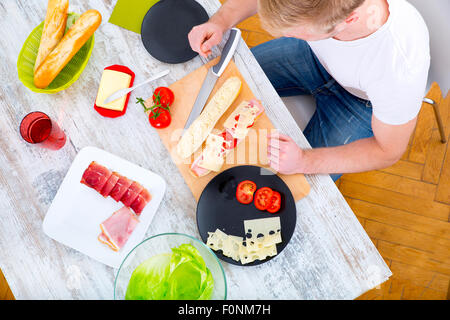 A young man preparing a sandwich in the kitchen. Stock Photo