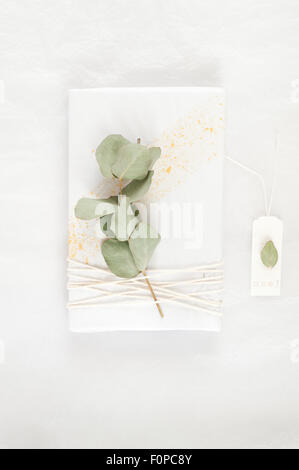 simple gift wrapping idea with white tissue paper splattered with gold paint decorated with twine and a sprig of eucalyptus Stock Photo