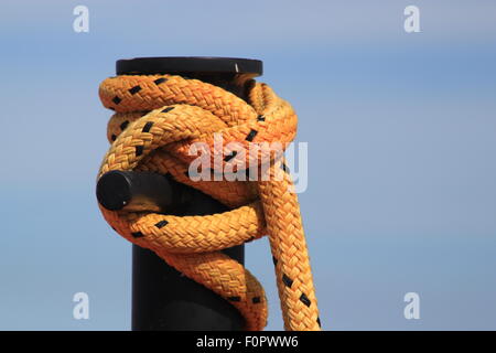 Yellow rope with black flecks tied around a large black post symbolising  security, securely fastened and safety Stock Photo
