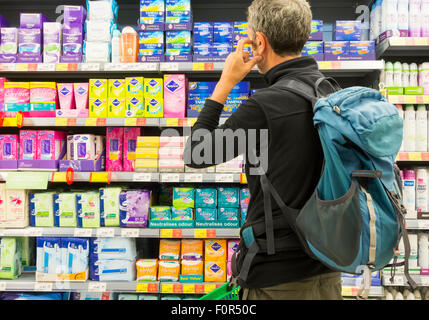 Middle aged man looking confused near feminine care products display in supermarket as he shops for tampons for partner Stock Photo