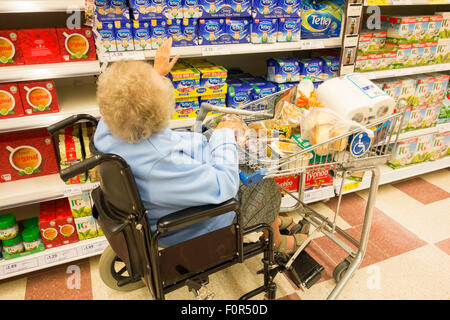 Elderly lady in her nineties with clip-on wheelchair trolley shopping in Tesco supermarket. England. UK Stock Photo