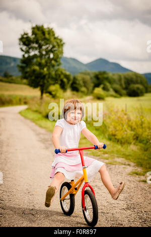 Little child driving her firs bicycle on rural road outdor in nature Stock Photo