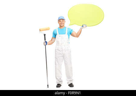 Young male house painter in a white jumpsuit holding a paint roller and a big yellow speech bubble isolated on white background Stock Photo