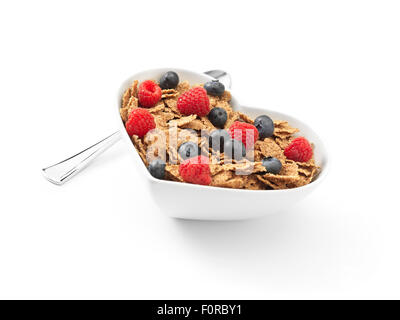 Angled shot of a heart shaped bowl of cereal with bran flakes covered in raspberries and blueberries on a pure white background Stock Photo