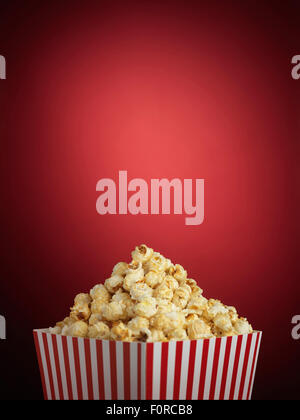 Shot of cinema style popcorn in a traditional striped box on a red background with a lot of copy space in a vignette or halo Stock Photo