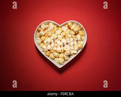 Shot of cinema style popcorn in a heart shaped bowl on a vibrant and bright red background with copy space and a clipping path. Stock Photo