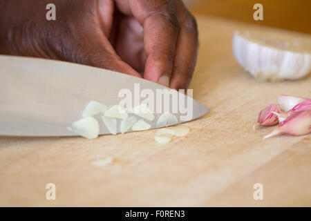 A black man chopping garlic on a wooden chopping board Stock Photo