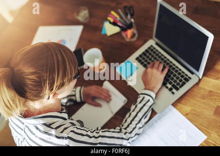 Young female entrepreneur working sitting at a desk typing on her laptop computer in a home office, view from above Stock Photo