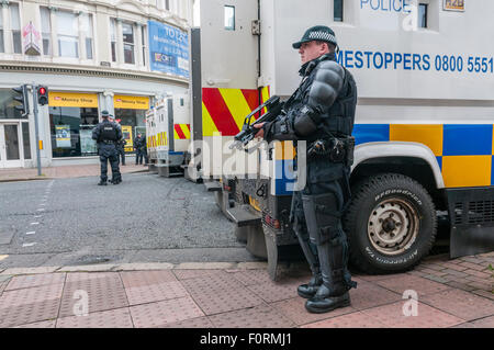 Armed PSNI police officer holds a Heckler & Koch G36C automatic machine gun on a street in Belfast as armoured cars block road Stock Photo