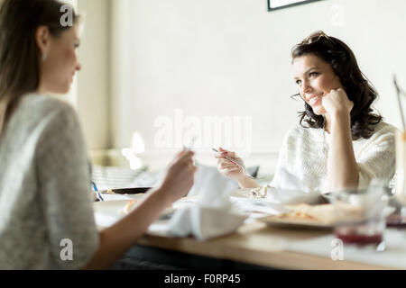 Two gorgeaus ladies eating in a restaurant while having a conversation Stock Photo