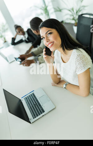 Happy and beautiful young businesswoman sitting at an office table and talking on her mobile phone Stock Photo