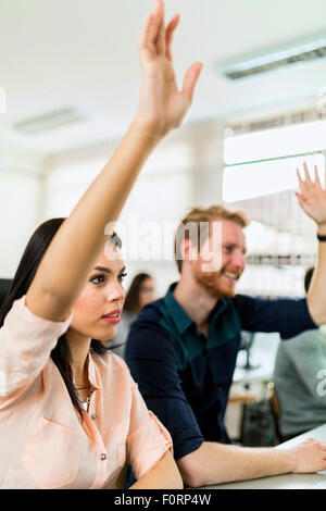 Beautiful young woman and a man raising hands in classroom in  while sitting at a desk Stock Photo