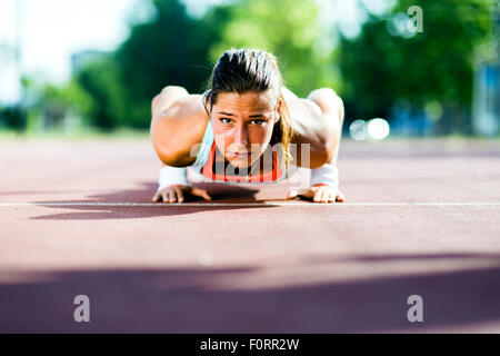 Focused young beautiful woman doing push-ups outdoors on a hot summer day Stock Photo