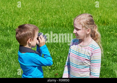Little boy with retro SLR camera shooting girl outdoors