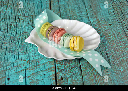 Row of colorful French macaroons on white seashell plate and polka dot ribbon. Stock Photo