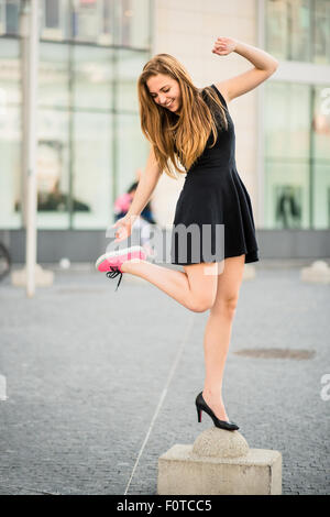 Which shoes to choose - teenager on street one foot in sneaker and other in high heel Stock Photo